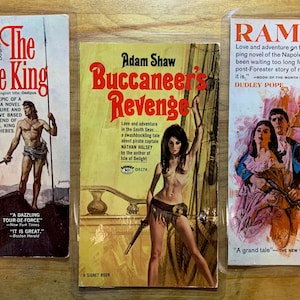 May include: Three vintage paperback books with colorful covers. Titles include "The Eagle King," "Buccaneer's Revenge," and "Ramage." The covers feature illustrations of historical and adventure themes, with text and imagery typical of mid-20th-century book design.