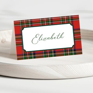 Puede incluir: Una tarjeta plegada con un patrón de cuadros rojos, verdes y blancos. La tarjeta tiene un centro blanco con un borde verde y el nombre "Elizabeth" en escritura verde. La tarjeta está sobre una bandeja blanca.