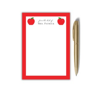 Puede incluir: Un bloc de notas blanco con borde rojo, con dos ilustraciones de manzanas rojas y el texto "from the desk of MRS. PATRICK." Un bolígrafo dorado descansa al lado. Ideal para profesores.