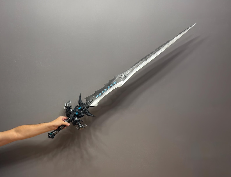 Pu&ograve; includere: Una grande spada fantasy argentata con intricati dettagli neri e blu. La lama &egrave; lunga e appuntita, con un'elsa decorativa. La spada &egrave; tenuta su uno sfondo grigio.