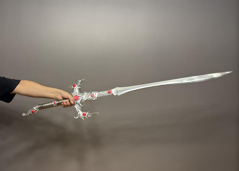 May include: A silver sword with a decorative handle and red gems. The sword is held by a person's hand.