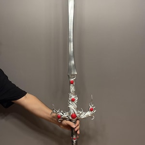 May include: A silver sword with a decorative, ornate handle. The handle is adorned with red gemstones. The sword has a sharp point and a double-edged blade.
