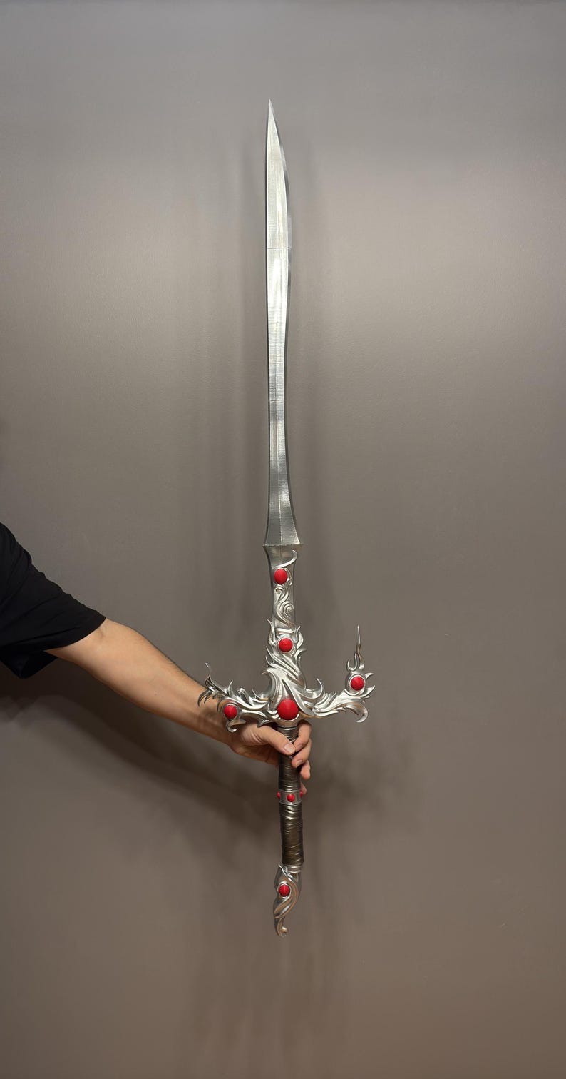 May include: A silver sword with a decorative, ornate handle. The handle is adorned with red gemstones. The sword has a sharp point and a double-edged blade.