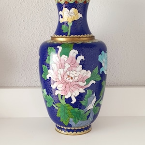 Pode incluir: Um vaso de cloisonné azul e dourado com um design floral. O vaso é decorado com flores rosa, brancas e verdes.