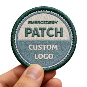 May include: A circular embroidered patch with a dark green scalloped border. The top half is off-white with the dark green text EMBROIDERY, and the bottom half is light blue with the white text PATCH, CUSTOM, and LOGO stacked vertically.