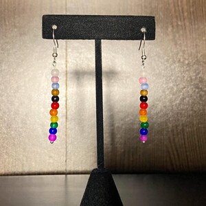 May include: A pair of rainbow beaded earrings with silver hooks. The beads are in the order of red, orange, yellow, green, blue, indigo, and violet.