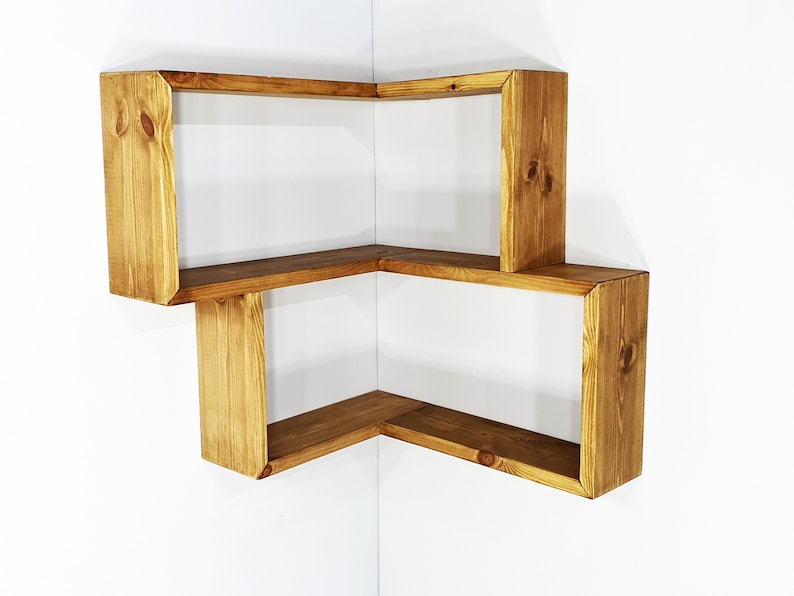May include: A wooden corner shelf unit with three shelves. The shelves are made of natural wood with a light brown stain. The shelves are in a corner of a room.
