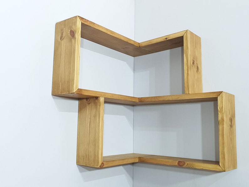 May include: A wooden corner shelf unit with three shelves. The shelves are made of natural wood with a light brown stain. The shelves are arranged in a staggered pattern, creating a unique and modern look.