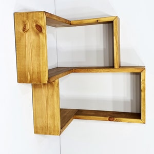 May include: A wooden corner shelf unit with three shelves. The shelves are made of natural wood with a light brown stain.