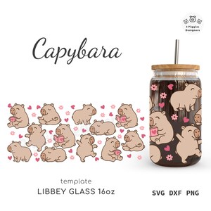 May include: A 16oz Libbey glass with a bamboo lid and metal straw, featuring a repeating pattern of cartoon capybaras, pink hearts, and small flowers. The design includes capybaras reading books, drinking from mugs, and sitting in poses.