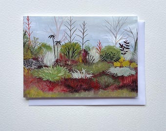May include: A greeting card featuring a colorful illustration of a garden scene. The artwork depicts various plants in shades of green, red, and yellow, with a light blue sky background. The card is set against a white envelope.