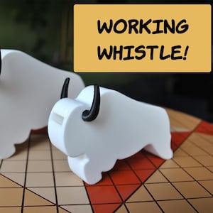 May include: Two white bison-shaped whistles with black horns. The whistles are on a checkered surface, and a yellow sign above them reads "WORKING WHISTLE!". The whistles are a fun, decorative item.