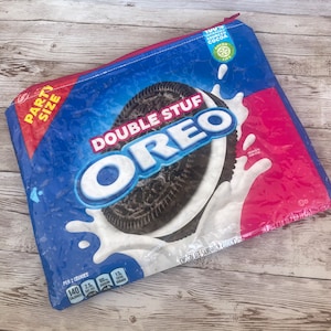 May include: A blue and pink zippered pouch with a large Oreo cookie graphic. The pouch has the text "Double Stuf Oreo" and "Party Size" printed on it. The pouch is made of a clear plastic material with a pink lining.
