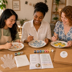 Könnte beinhalten: Drei Personen bemalen Keramikteller mit Blumen- und Zitrusmotiven. Farbe, Pinsel und ein Set mit Anweisungen liegen auf dem Tisch. Das Set enthält den Text "Let's Get Started" und "My Ceramic Plate Painting Kit".