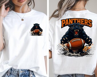 May include: White t-shirt featuring a black panther graphic holding a football. The front has a small panther graphic, while the back displays a larger design with the word "PANTHERS" in orange. A sports-themed apparel item.