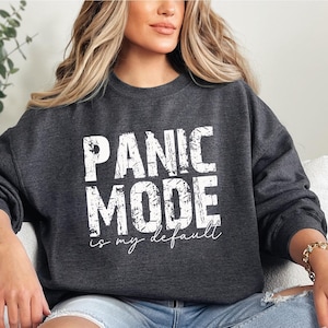 May include: Dark gray sweatshirt with the text "PANIC MODE is my default" in white block letters. The sweatshirt is a crew neck style and appears to be made of a soft material. The text is in a distressed font.