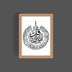 May include: A framed print of black Arabic calligraphy in a circular design on a white background. The calligraphy is in a decorative style and includes the phrase "Allah" in the center.