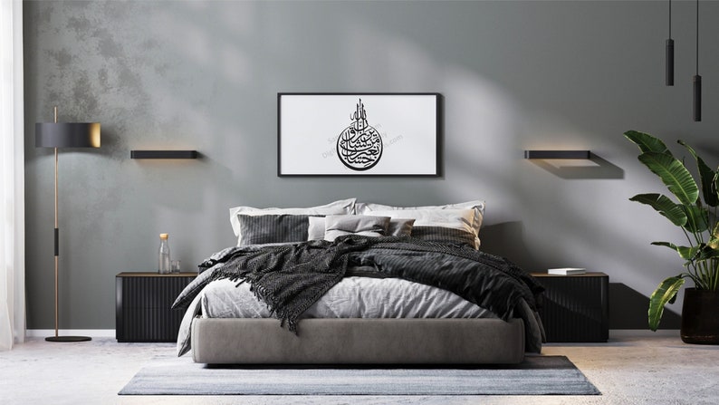 May include: A modern bedroom with a gray wall, a bed with black and white bedding, a black and white framed print with Arabic calligraphy, and two black wall sconces.