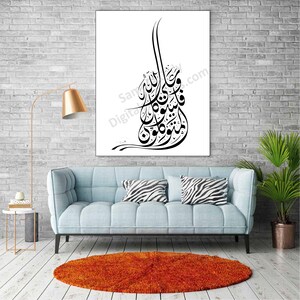 Op de afbeelding: Een zwart-wit kalligrafiekunstprint met Arabische schrift op een witte achtergrond. De print is ingelijst en hangt aan een witte bakstenen muur boven een lichtblauwe bank met zebraprint kussens.