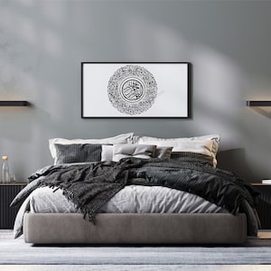 May include: A modern bedroom with a gray wall, a black bed frame, and a black and white framed print of Arabic calligraphy. The bed has a gray headboard and a black blanket. There are two black nightstands on either side of the bed.