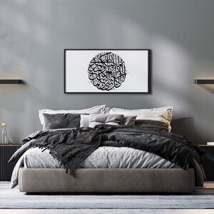 May include: A modern bedroom with a gray wall, a bed with a gray headboard and a black blanket, two black nightstands, a black floor lamp, two black wall sconces, a framed black and white print of Arabic calligraphy, and a potted green plant.