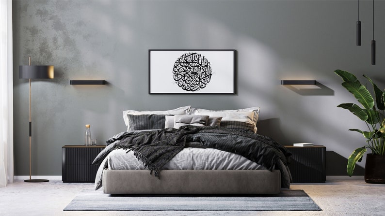 May include: A modern bedroom with a gray wall, a bed with a gray headboard and a black blanket, two black nightstands, a black floor lamp, two black wall sconces, a framed black and white print of Arabic calligraphy, and a potted green plant.