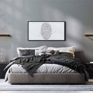 Op de afbeelding: Een moderne slaapkamer met een grijze muur, een bed met zwart en grijs beddengoed, een zwarte staande lamp met gouden accenten en een ingelijst afdruk met zwarte Arabische kalligrafie op een witte achtergrond.