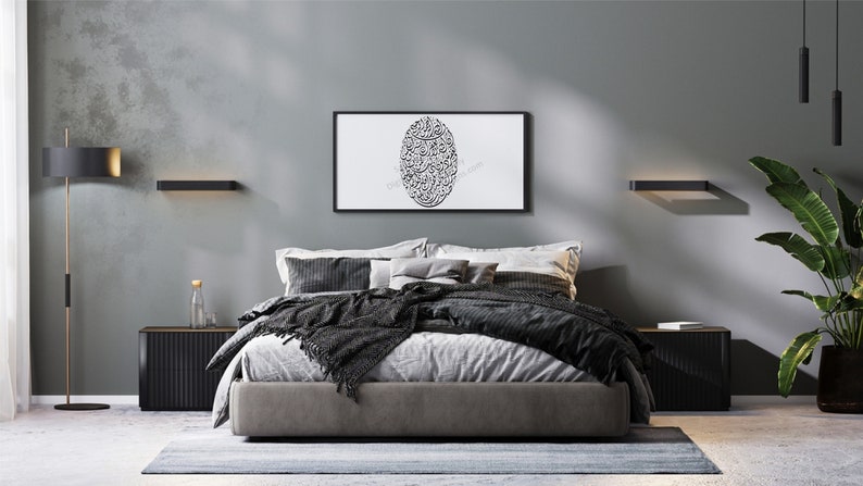 Op de afbeelding: Een moderne slaapkamer met een grijze muur, een bed met zwart en grijs beddengoed, een zwarte staande lamp met gouden accenten en een ingelijst afdruk met zwarte Arabische kalligrafie op een witte achtergrond.