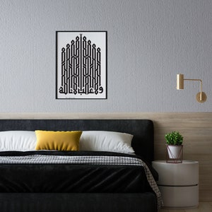 May include: A black and white framed print of Arabic calligraphy in a geometric pattern, hanging on a gray wall above a black headboard with a yellow throw pillow and a white bedspread.