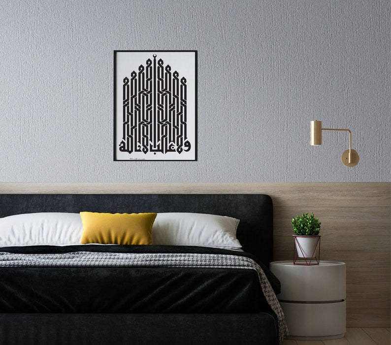 May include: A black and white framed print of Arabic calligraphy in a geometric pattern, hanging on a gray wall above a black headboard with a yellow throw pillow and a white bedspread.