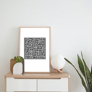 May include: A black and white framed print of Islamic calligraphy in a square shape. The print is hanging on a white wall above a white dresser with two drawers. A small potted plant and a white lamp are on the dresser.