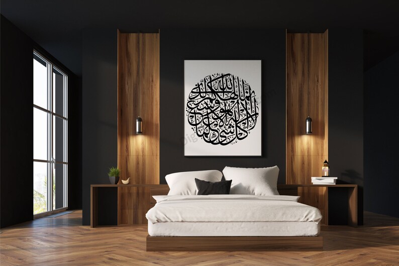 May include: A black and white calligraphy artwork of Islamic text hangs above a white bed with black and white pillows in a modern bedroom with dark walls and wood paneling.
