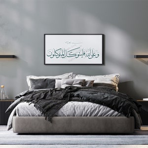 Op de afbeelding: Een slaapkamer met een grijze muur, een bed met een grijs hoofdeinde en zwarte beddengoed, een zwart nachtkastje, een zwarte staande lamp en een ingelijst afdruk met Arabische kalligrafie die "Wa alaa alladhina amanoo wa amiloo al-salihati" luidt