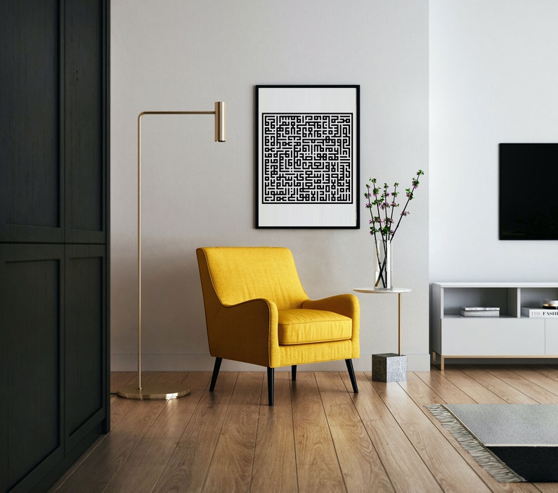 May include: A yellow armchair with black legs sits in a living room with a black and white framed print on the wall, a gold floor lamp, a small table with a vase of flowers, and a white entertainment center with a television.