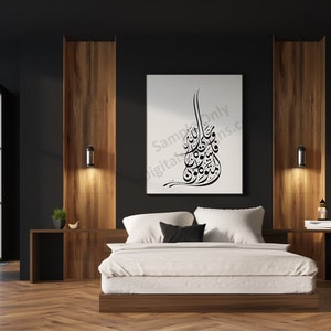 Op de afbeelding: Een witte canvasprint met zwarte Arabische kalligrafie hangt boven een wit bed met een zwart hoofdeinde in een moderne slaapkamer met donker houten lambrisering en een groot raam.