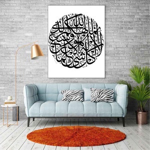 May include: Black and white Islamic calligraphy art print with a circular design. The print is framed and hanging on a white brick wall above a light blue sofa.
