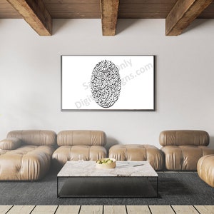 Op de afbeelding: Een zwart-wit kalligrafie kunstprint in een zwart frame hangend aan een witte muur boven een bruine leren sectionele bank. De bank staat in een woonkamer met een houten vloer en een salontafel met een fruitschaal erop.