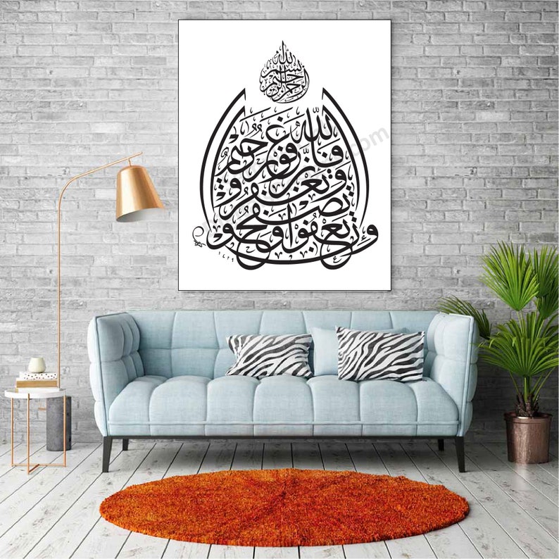 May include: A black and white Islamic calligraphy art print featuring Arabic script in a circular design. The print is framed and hanging on a white brick wall above a light blue sofa with zebra print throw pillows.