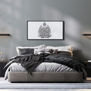 May include: A modern bedroom with a gray bed, black nightstands, and a black and white framed print of Arabic calligraphy on the wall. The room has a gray wall, a black floor lamp, and a potted plant.
