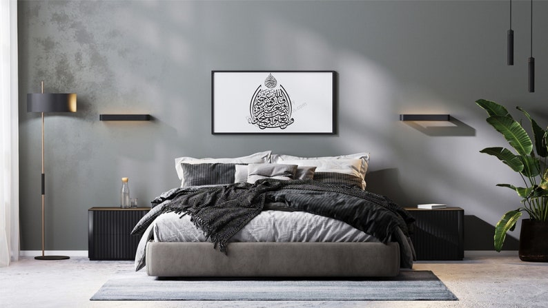 May include: A modern bedroom with a gray bed, black nightstands, and a black and white framed print of Arabic calligraphy on the wall. The room has a gray wall, a black floor lamp, and a potted plant.