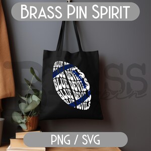 May include: Black tote bag with a white and blue football graphic. The graphic features the words "BLUE DEVILS" in a repeating pattern. The text "BRASS PIN SPIRIT" is at the top, and "PNG / SVG" is at the bottom.