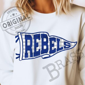 May include: A white crewneck sweatshirt featuring a graphic of a blue and white checkered pennant flag. The word REBELS is printed in bold blue capital letters across the center of the pennant. The design includes blue ties on the left side.