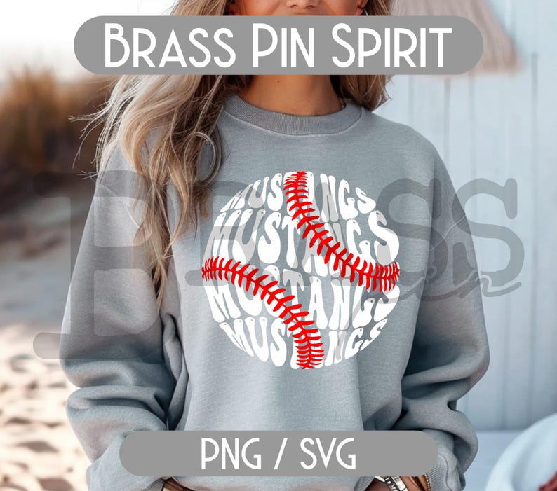 Puede incluir: Una sudadera gris con un dise&ntilde;o de b&eacute;isbol. El gr&aacute;fico de b&eacute;isbol presenta la palabra "Mustangs" en un patr&oacute;n circular, con detalles de costura rojos. El texto "Brass Pin Spirit" est&aacute; encima del dise&ntilde;o.