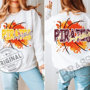 May include: White sweatshirt with a basketball graphic. The front features the word "PIRATES" in yellow and the word "basketball" in a script font, over an orange and yellow splatter design. The back has the same design, but the word "PIRATES" is in maroon.