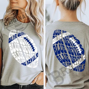 May include: A gray t-shirt featuring a blue and white football design. The football graphic is filled with the words "BLUE DEVILS". The image shows both the front and back of the shirt.