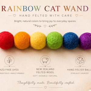 May include: A rainbow cat wand with six felted wool balls in red, orange, yellow, green, blue, and purple. The text reads "RAINBOW CAT WAND" and "HAND FELTED WITH CARE". The wand is made with Azo-free dyes and ethically sourced materials.