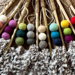 May include: A selection of cat toys featuring wooden sticks, colourful felt balls, and fluffy grey and white feather attachments. The felt balls are in shades of pink, purple, green, and yellow.