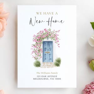 May include: A white card featuring the text "WE HAVE A New Home" above a watercolour illustration of a blue door with pink flowers. The address and family name are printed below.
