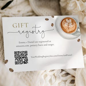 Pode incluir: Um cartão branco de registro de presentes com as palavras "GIFT registry" em escrita dourada e preta. O cartão apresenta uma ilustração em aquarela de uma xícara de café com arte latte e grãos de café espalhados. O texto "Emma + Daniel are registered at amazon.com, pottery barn and target" também está incluído.