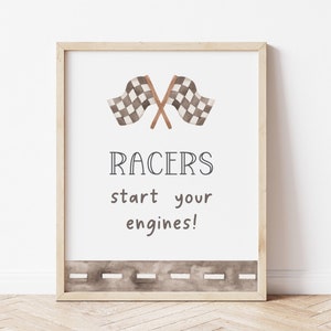 May include: A printable wall art print with a watercolor illustration of two checkered flags crossed over each other. The text "RACERS start your engines!" is below the flags. A brown dashed line is at the bottom of the print.